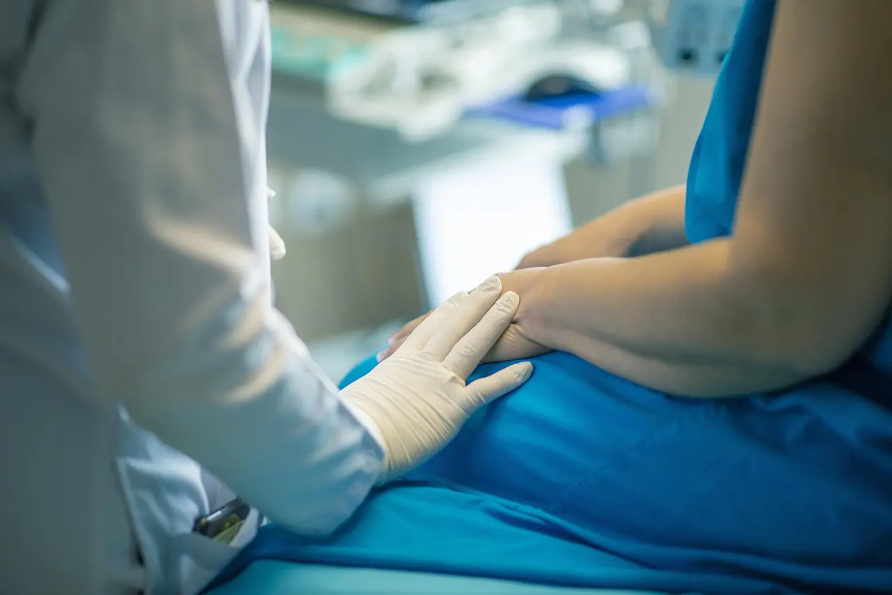 Doctor comforting patient by holding their hands in a clinical setting.