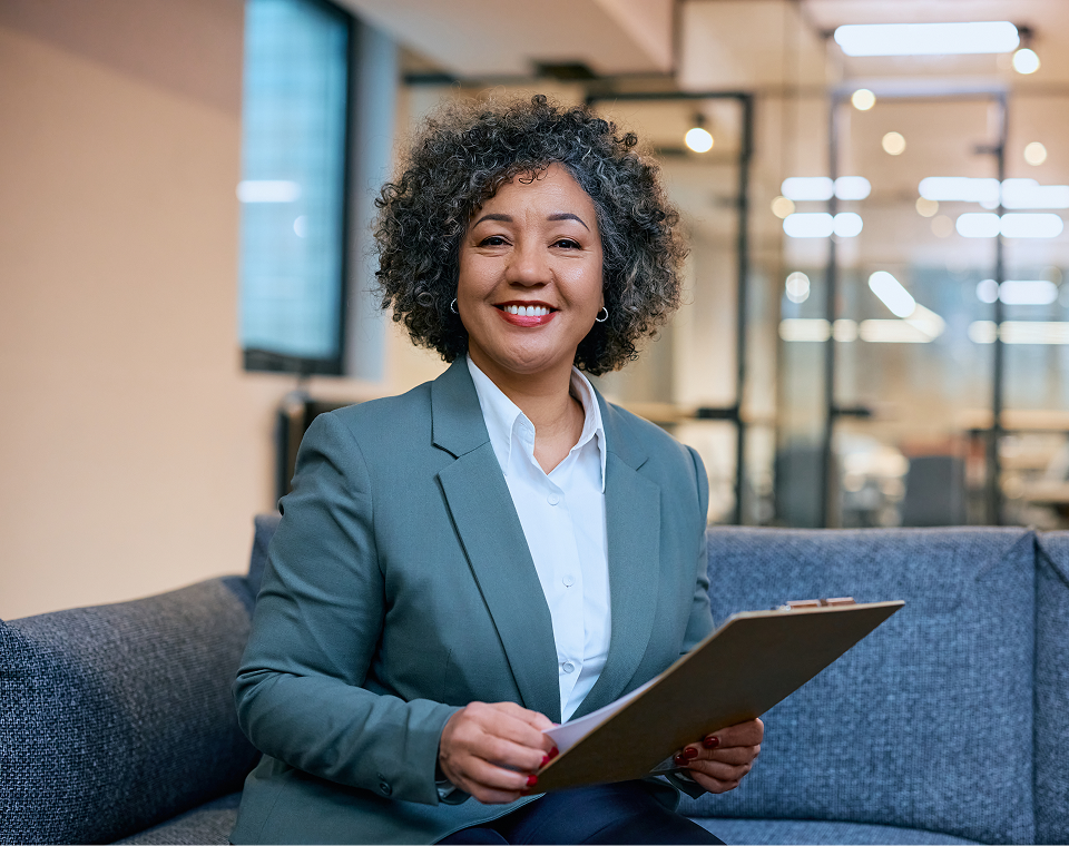 Confident businesswoman holding a clipboard, smiling in a modern office.